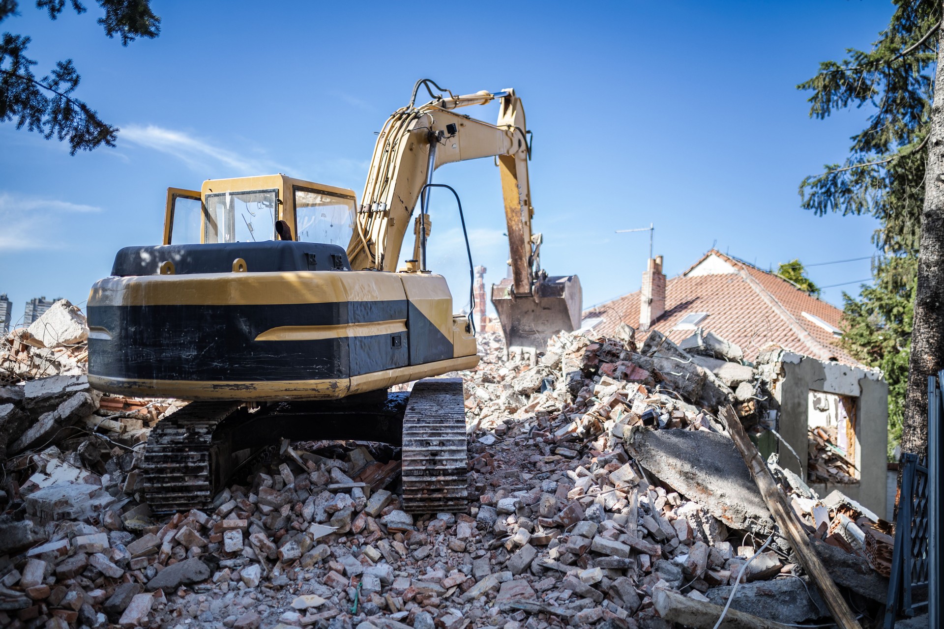 Excavator clearing rubble from demolished building site under clear blue sky