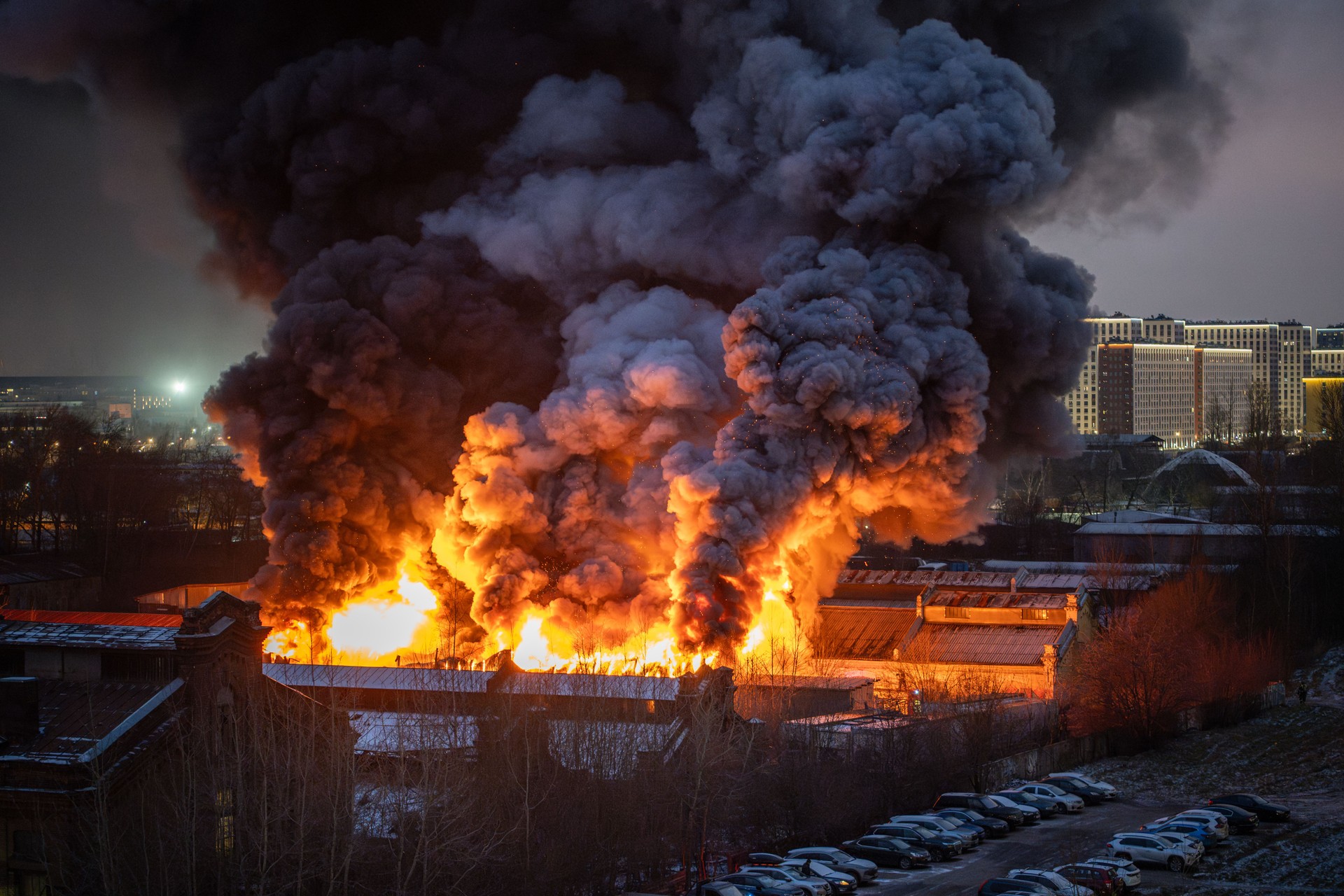 Nearby burning building with orange flames, parks and smoke from fire in residential house at night.