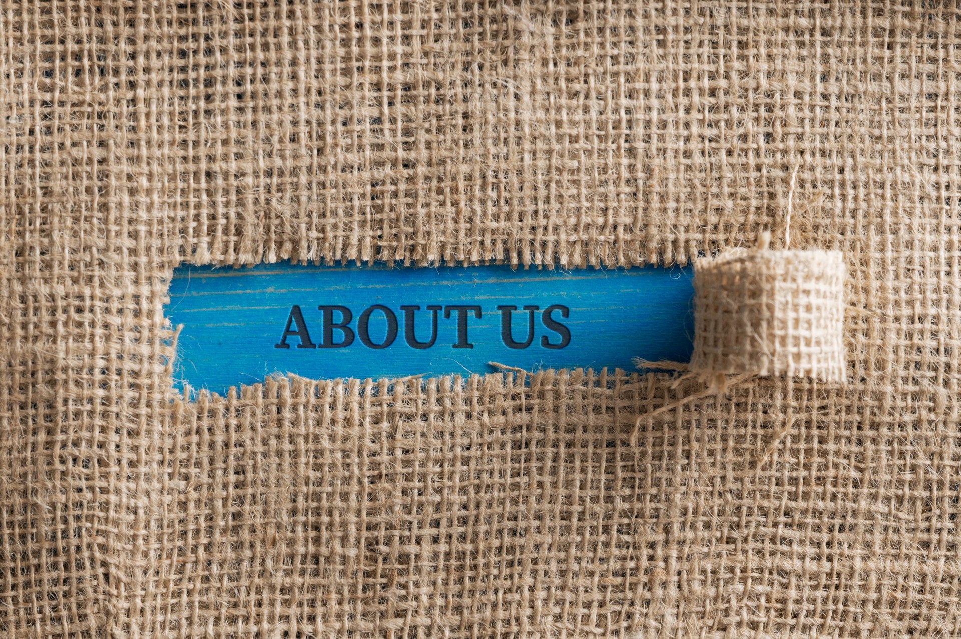 Top view of a rough linen fabric with a torn window in the middle with an About us  sign in it